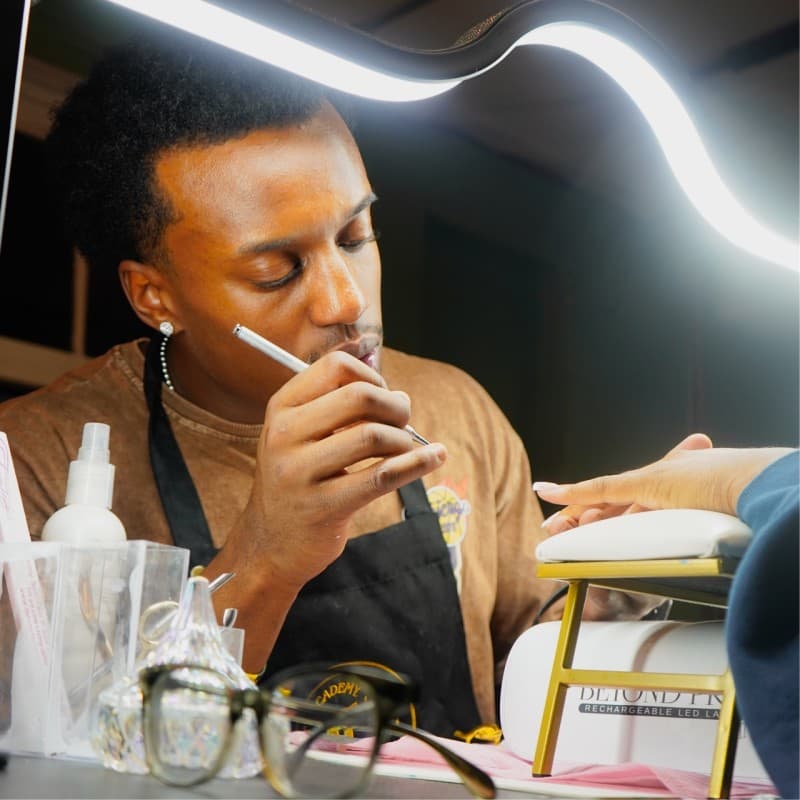 Jayden Pean working on a client's nails under the lamp, focused and precise.